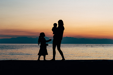 Silhouette of a parent with two children against sunset over a lake | SV Partners