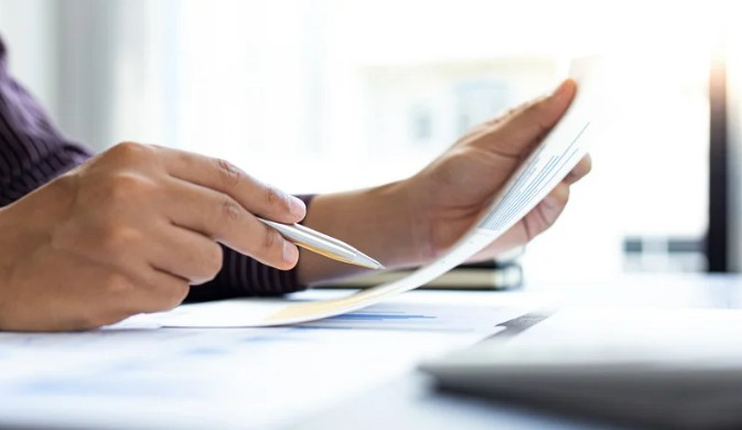 Person holding a document and a pen in their hands